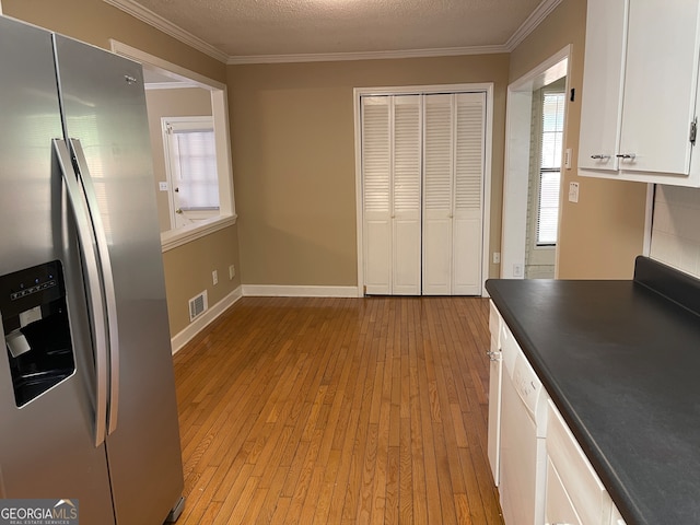 kitchen featuring light wood-type flooring, crown molding, stainless steel fridge, white cabinetry, and a textured ceiling