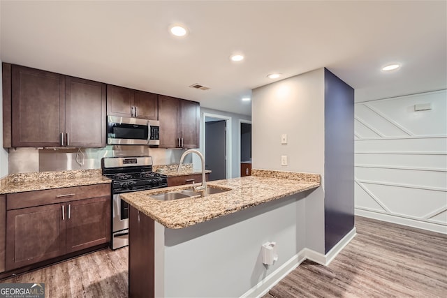 kitchen with appliances with stainless steel finishes, light hardwood / wood-style floors, kitchen peninsula, and sink