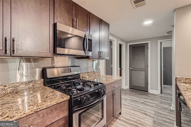 kitchen featuring light wood-type flooring, appliances with stainless steel finishes, light stone countertops, and dark brown cabinetry