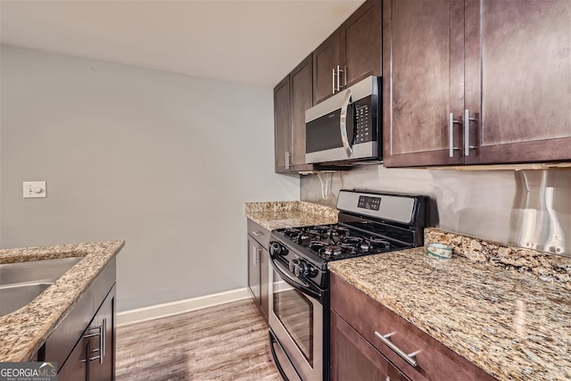 kitchen featuring light wood-type flooring, appliances with stainless steel finishes, light stone counters, and dark brown cabinetry