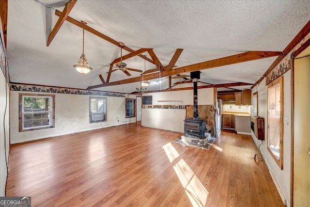 unfurnished living room with vaulted ceiling with beams, a wood stove, and a textured ceiling