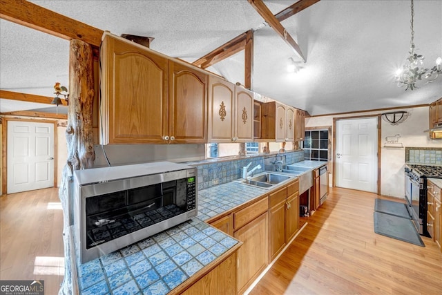 kitchen with vaulted ceiling with beams, light hardwood / wood-style floors, a textured ceiling, and appliances with stainless steel finishes