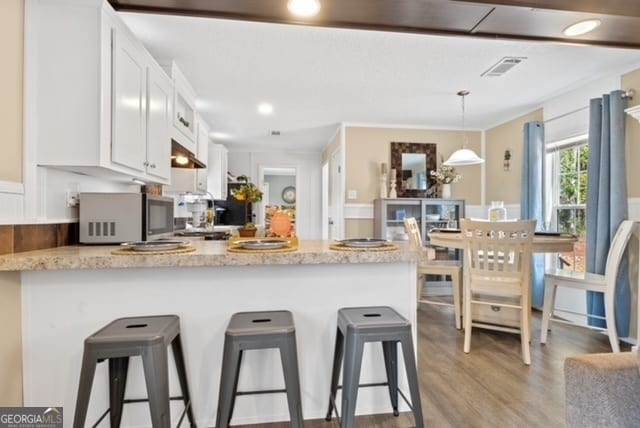 kitchen featuring light hardwood / wood-style floors, white cabinetry, kitchen peninsula, a kitchen bar, and hanging light fixtures