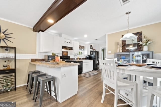 kitchen with white cabinets, kitchen peninsula, a breakfast bar area, pendant lighting, and light hardwood / wood-style flooring