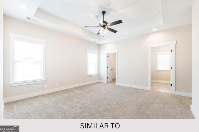 unfurnished bedroom featuring a tray ceiling, ceiling fan, light colored carpet, and ensuite bathroom