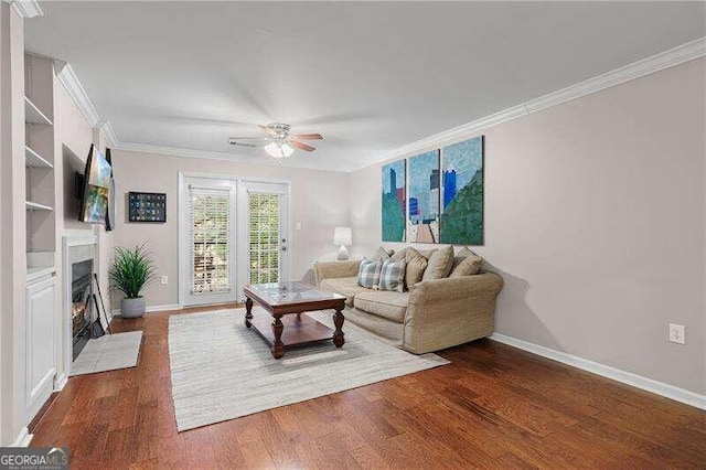 living area featuring baseboards, a fireplace with flush hearth, ornamental molding, dark wood-style floors, and a ceiling fan