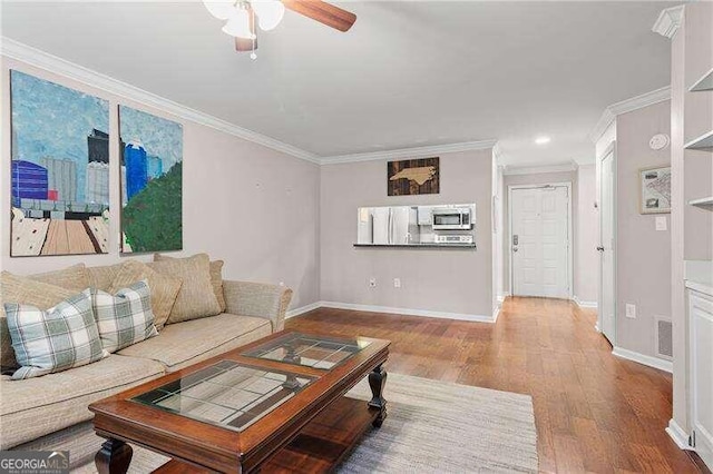 living room featuring a ceiling fan, crown molding, wood finished floors, and baseboards