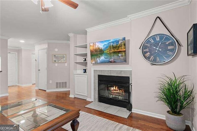 living area with visible vents, crown molding, a ceiling fan, and wood finished floors