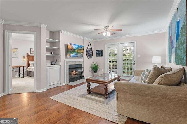 living area featuring built in shelves, ornamental molding, wood finished floors, a fireplace, and ceiling fan