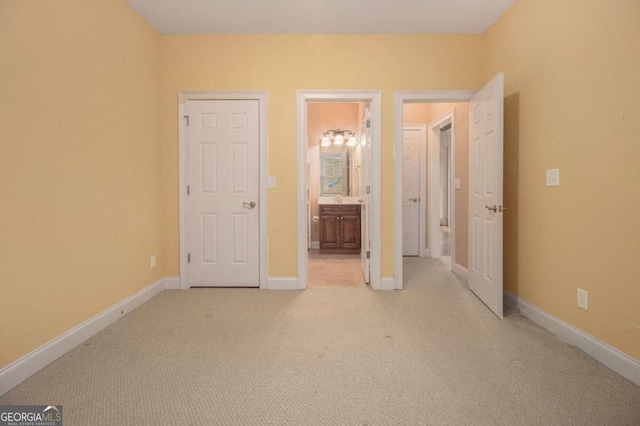 unfurnished bedroom with multiple windows, a walk in closet, ensuite bathroom, and light colored carpet