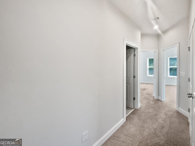 hallway featuring visible vents, carpet, and baseboards