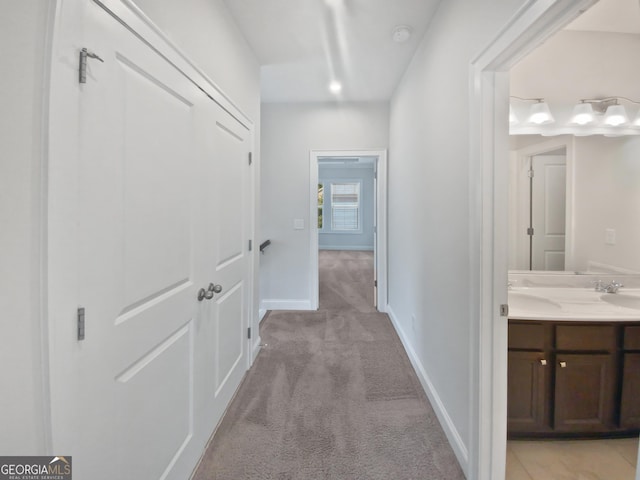 corridor featuring light colored carpet, baseboards, and a sink