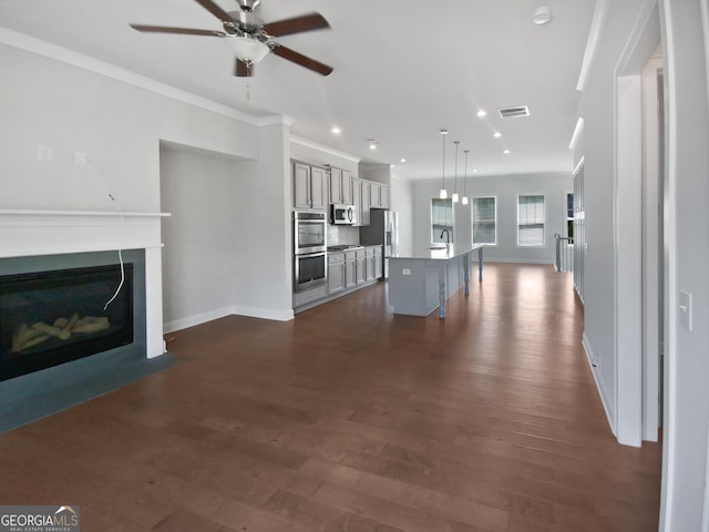 unfurnished living room with visible vents, ceiling fan, dark wood finished floors, ornamental molding, and a glass covered fireplace