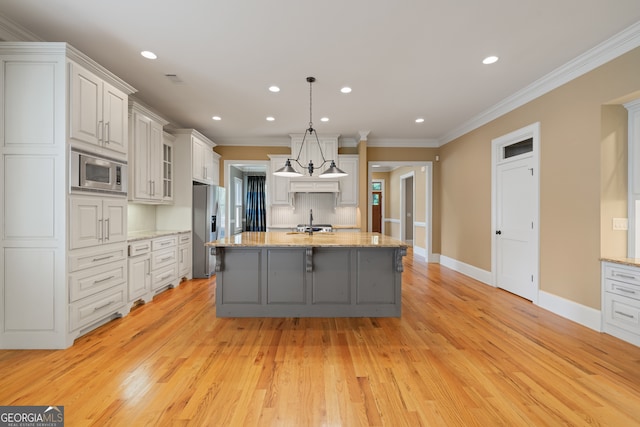 kitchen featuring white cabinets, decorative light fixtures, light wood-type flooring, appliances with stainless steel finishes, and a kitchen island with sink