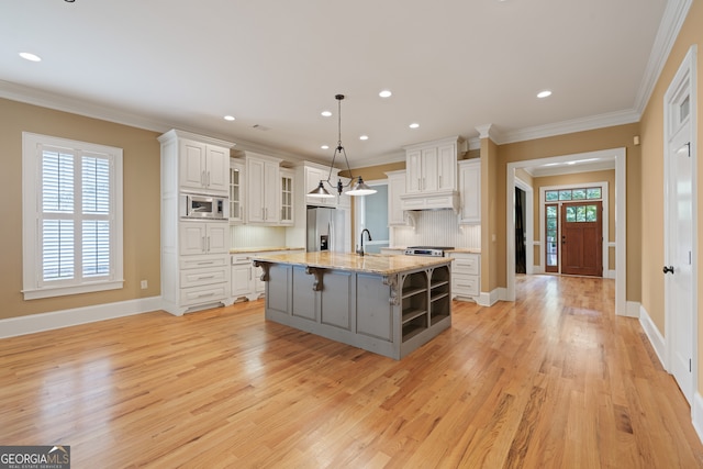 kitchen featuring a kitchen island with sink, light hardwood / wood-style flooring, stainless steel appliances, hanging light fixtures, and white cabinets