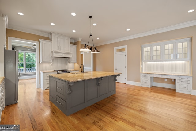 kitchen with pendant lighting, stainless steel appliances, ceiling fan, a center island with sink, and white cabinets