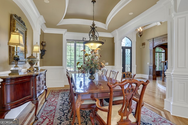 dining area with crown molding, light hardwood / wood-style flooring, ornate columns, and an inviting chandelier