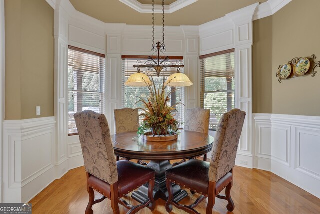 dining area featuring a wainscoted wall, a decorative wall, crown molding, light wood-style floors, and a tray ceiling