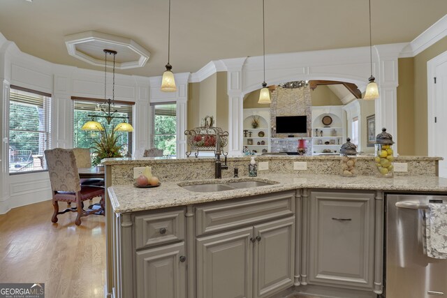 kitchen featuring light stone countertops, stainless steel dishwasher, hanging light fixtures, sink, and light wood-type flooring