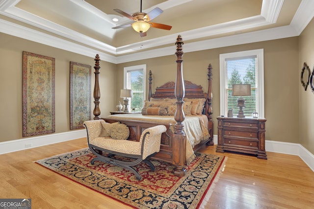 bedroom featuring light wood-type flooring, multiple windows, a tray ceiling, and ceiling fan