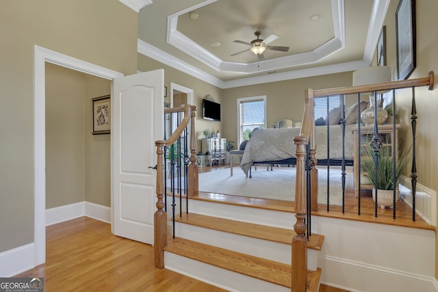 stairway featuring crown molding, ceiling fan, hardwood / wood-style floors, and a tray ceiling