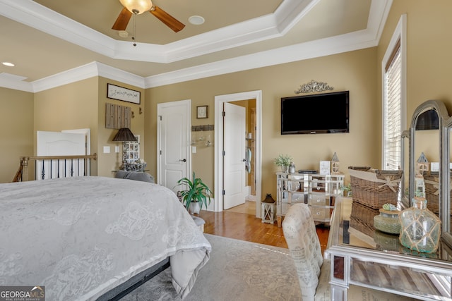 bedroom featuring ornamental molding, light hardwood / wood-style flooring, a tray ceiling, and ceiling fan