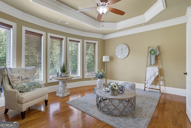 sitting room with hardwood / wood-style floors, ceiling fan, a tray ceiling, and ornamental molding