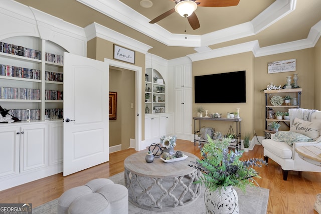 living room with ceiling fan, ornamental molding, a raised ceiling, and light hardwood / wood-style flooring