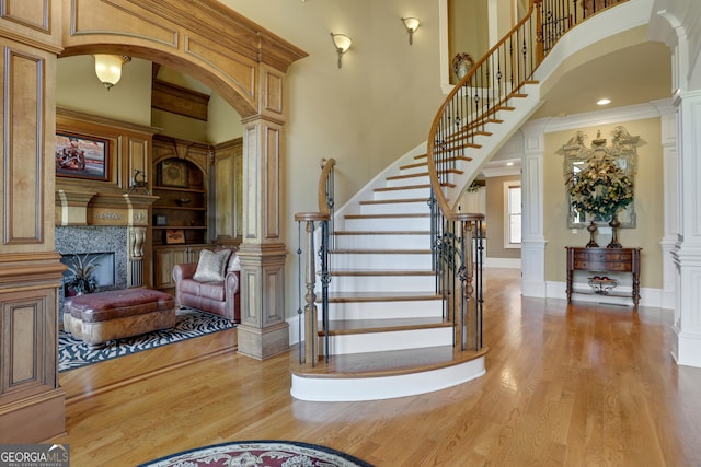 foyer entrance with a towering ceiling, crown molding, light hardwood / wood-style flooring, and decorative columns