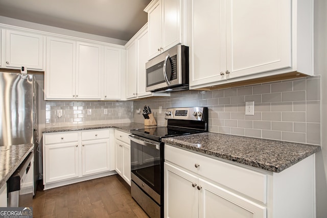 kitchen with dark stone countertops, backsplash, stainless steel appliances, white cabinetry, and dark wood-type flooring