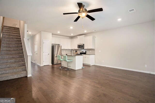 kitchen with a kitchen island with sink, a kitchen bar, stainless steel appliances, ceiling fan, and white cabinets