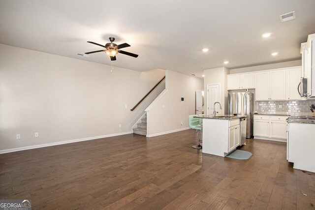 kitchen with white cabinets, appliances with stainless steel finishes, dark hardwood / wood-style flooring, ceiling fan, and a center island with sink