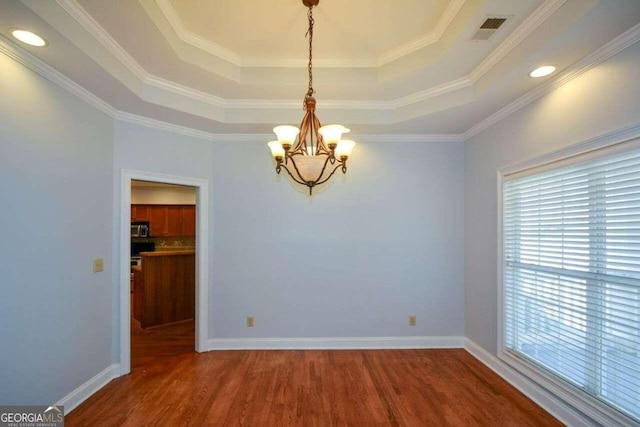 empty room with a tray ceiling, hardwood / wood-style flooring, crown molding, and a notable chandelier