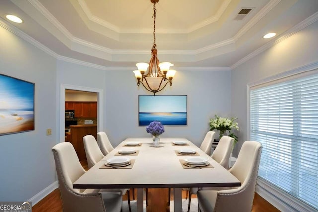 dining area featuring a raised ceiling, ornamental molding, dark hardwood / wood-style flooring, and a notable chandelier