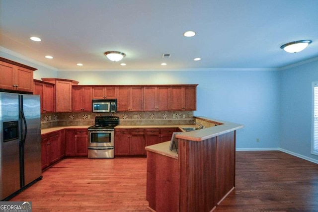 kitchen featuring hardwood / wood-style floors, tasteful backsplash, crown molding, stainless steel appliances, and kitchen peninsula