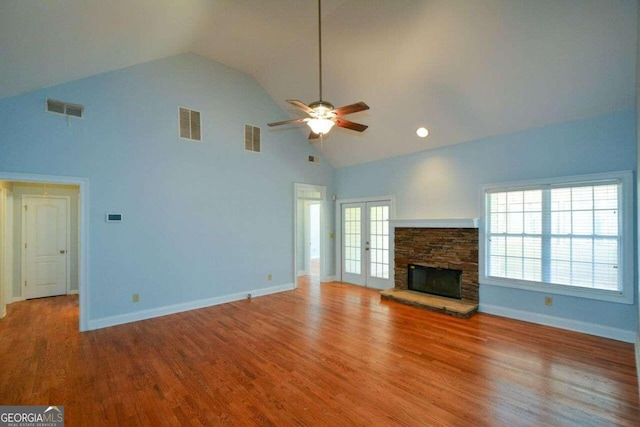 unfurnished living room with french doors, high vaulted ceiling, light hardwood / wood-style floors, a stone fireplace, and ceiling fan