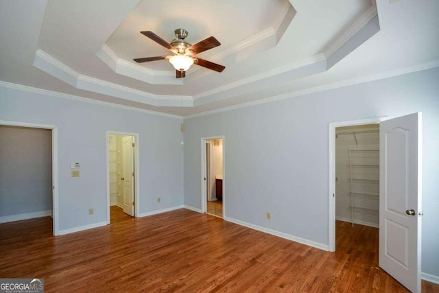 unfurnished bedroom featuring a walk in closet, wood-type flooring, ensuite bathroom, and ceiling fan