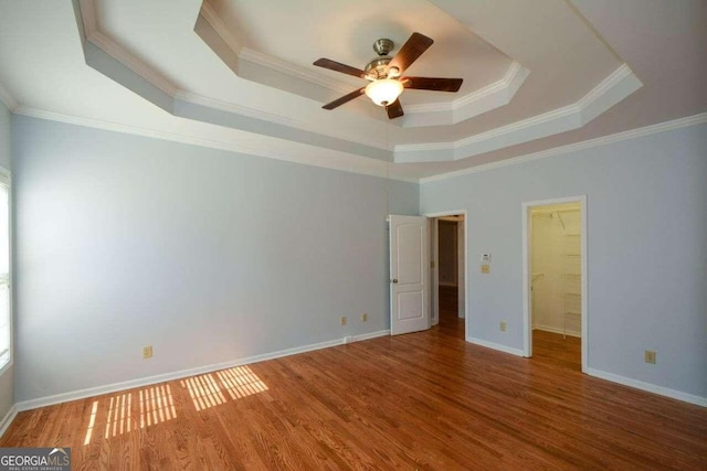 empty room with hardwood / wood-style floors, ceiling fan, a raised ceiling, and ornamental molding