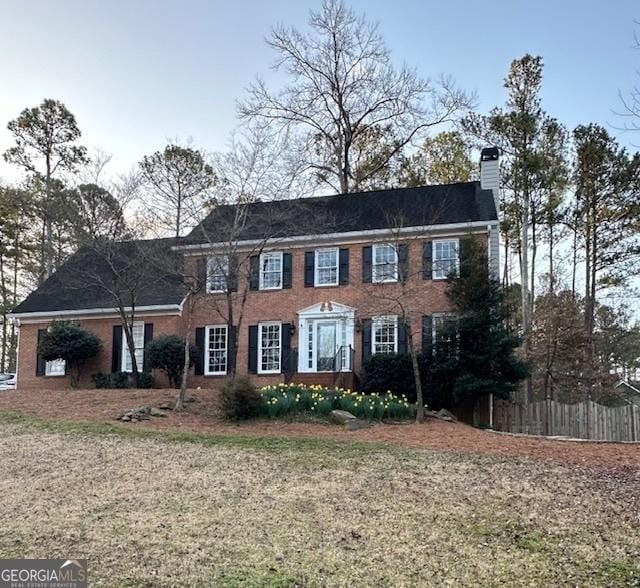 colonial house with brick siding, a front yard, a chimney, and fence