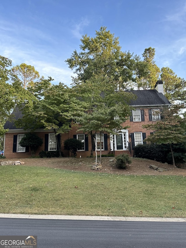 colonial-style house featuring brick siding, a chimney, and a front yard