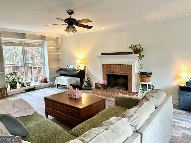 living area with built in shelves, a ceiling fan, wood finished floors, a fireplace, and crown molding