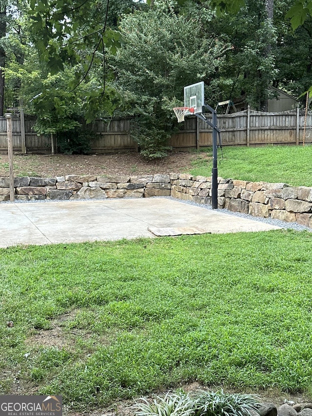 view of basketball court featuring basketball hoop, a lawn, and a fenced backyard