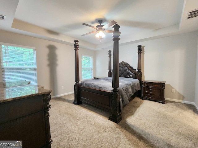 bedroom featuring multiple windows, a tray ceiling, light carpet, and ceiling fan