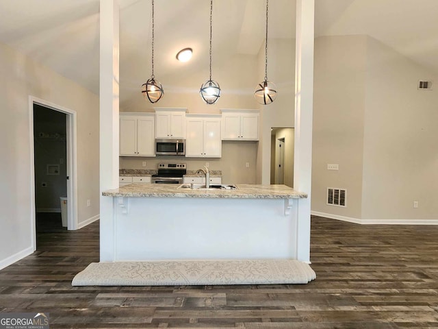 kitchen with white cabinets, hanging light fixtures, appliances with stainless steel finishes, light stone counters, and dark wood-type flooring