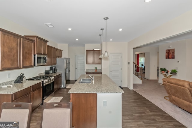 kitchen featuring a center island with sink, appliances with stainless steel finishes, hanging light fixtures, sink, and light stone counters