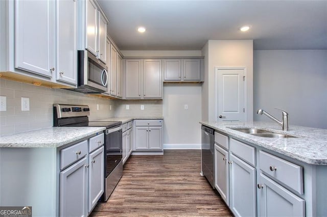 kitchen with light stone counters, dark wood-type flooring, sink, gray cabinetry, and stainless steel appliances