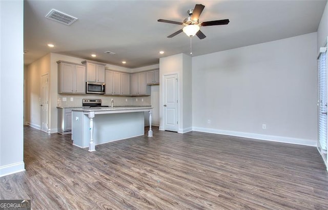 kitchen with gray cabinets, dark wood-type flooring, a center island with sink, appliances with stainless steel finishes, and ceiling fan