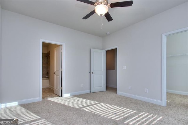 unfurnished bedroom featuring a closet, light colored carpet, ensuite bath, a walk in closet, and ceiling fan