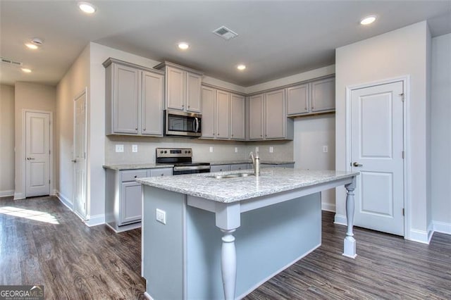 kitchen with appliances with stainless steel finishes, gray cabinetry, a kitchen island with sink, and dark hardwood / wood-style flooring