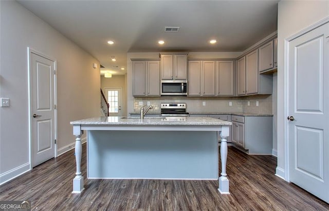 kitchen with a kitchen island with sink, appliances with stainless steel finishes, dark wood-type flooring, and decorative backsplash